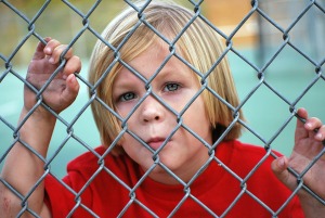 young Caucasian blonde boy stuck on the other side of the fence